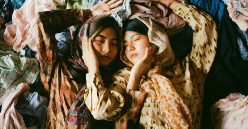 Scarves - Two Women Wearing Earth-toned Printed Tops And Scarves Lying On A Pile Of Clothes