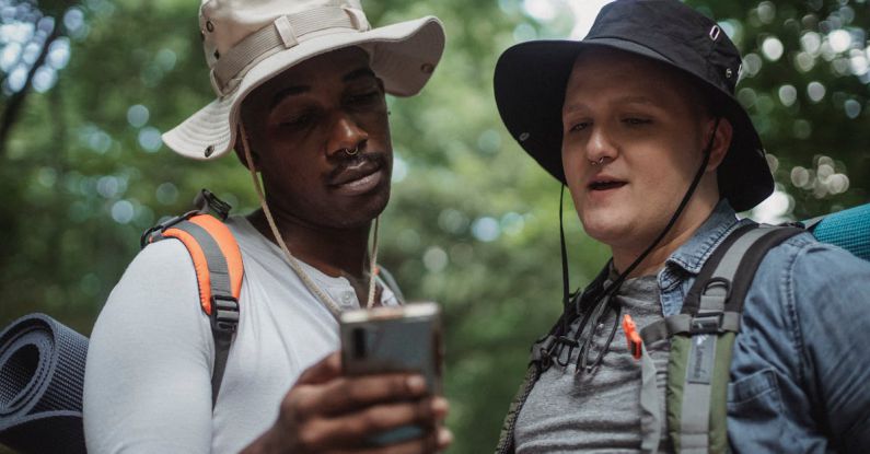 Watch - Young multiethnic hikers with backpacks watching cellphone against trees while spending time together on weekend